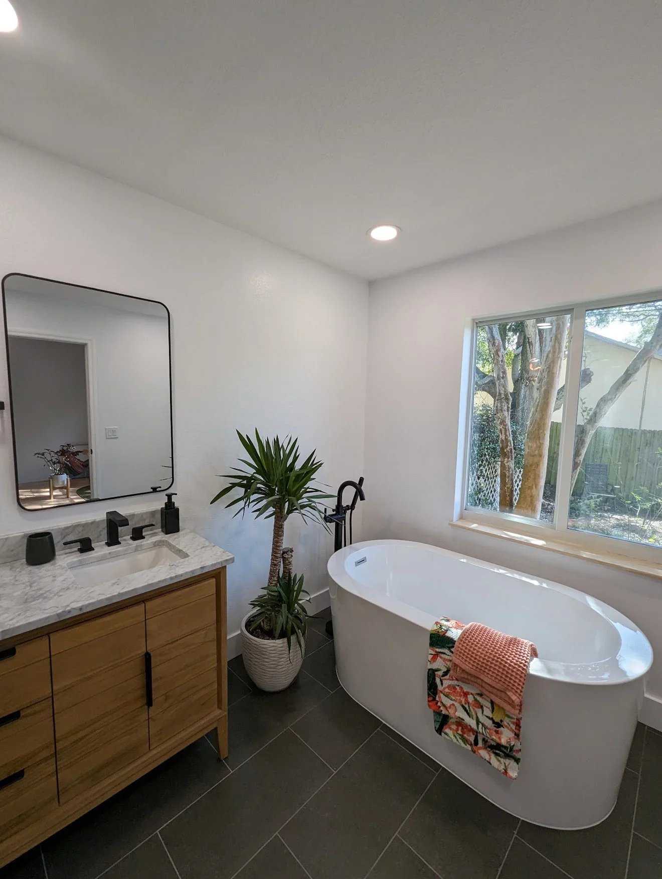 Modern bathroom with freestanding tub, marble counters, wood vanity, and tile flooring