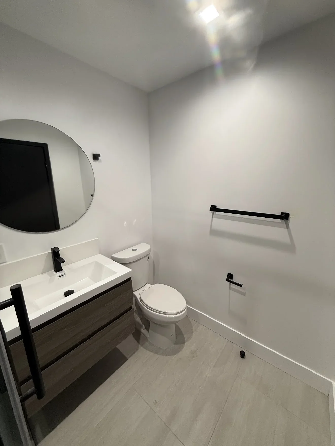 Modern bathroom with white quartz vanity, dark cabinetry, round mirror, and gray tile flooring
