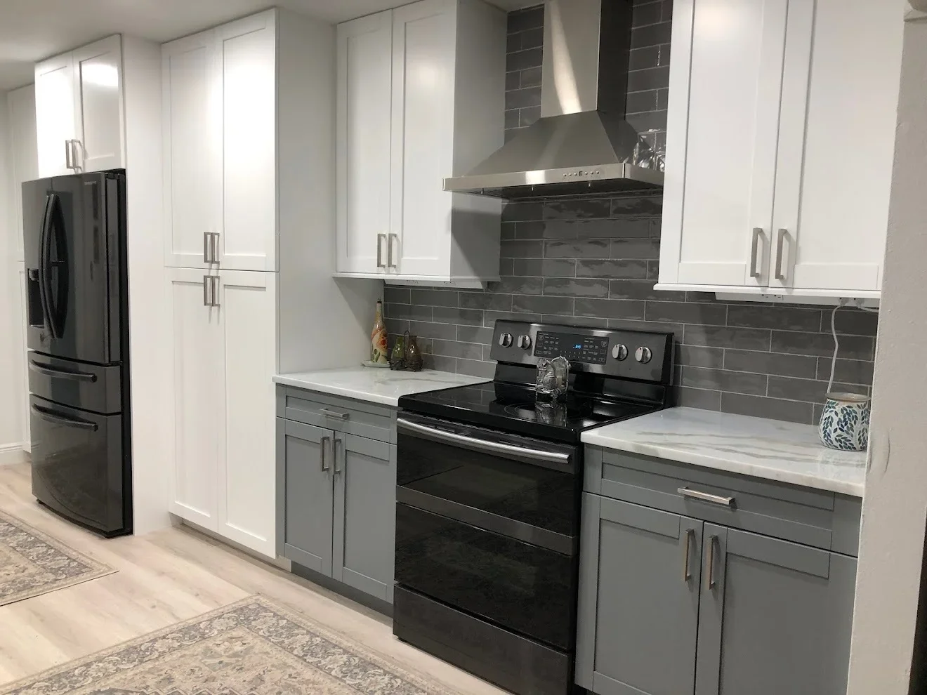 Modern kitchen with white and gray cabinetry, dark subway tile backsplash, black appliances, and quartz counters
