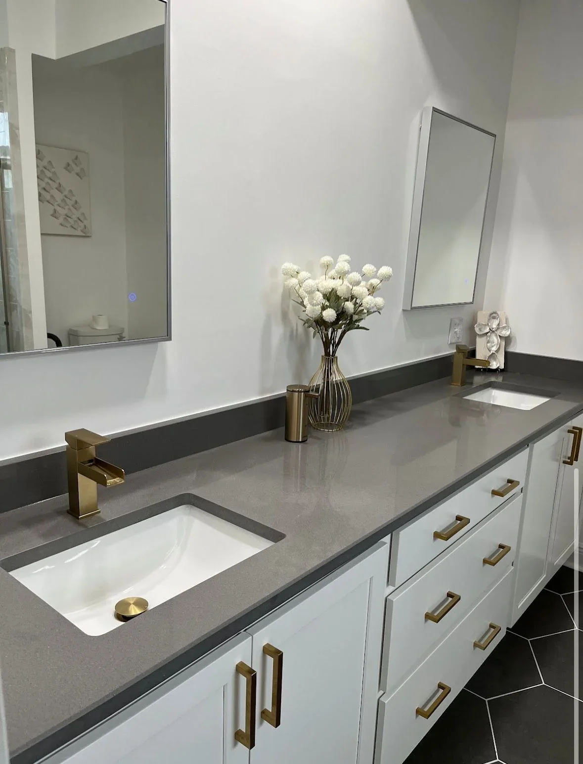 Gray quartz countertop with white undermount sink, white cabinetry, brass fixtures and hardware, dual mirrors