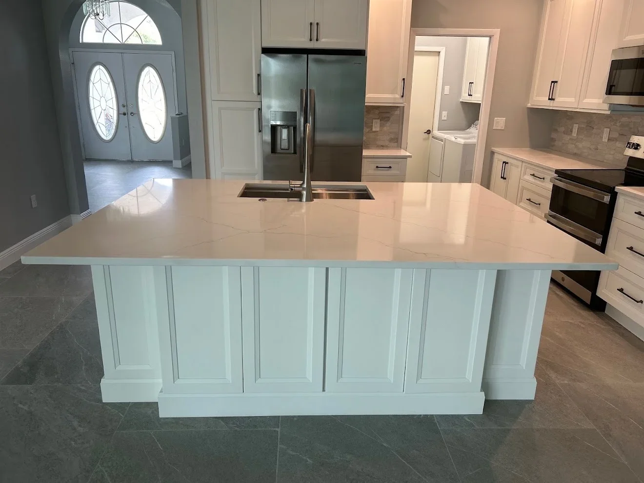 White kitchen cabinetry with quartz waterfall island, stainless steel appliances and sink