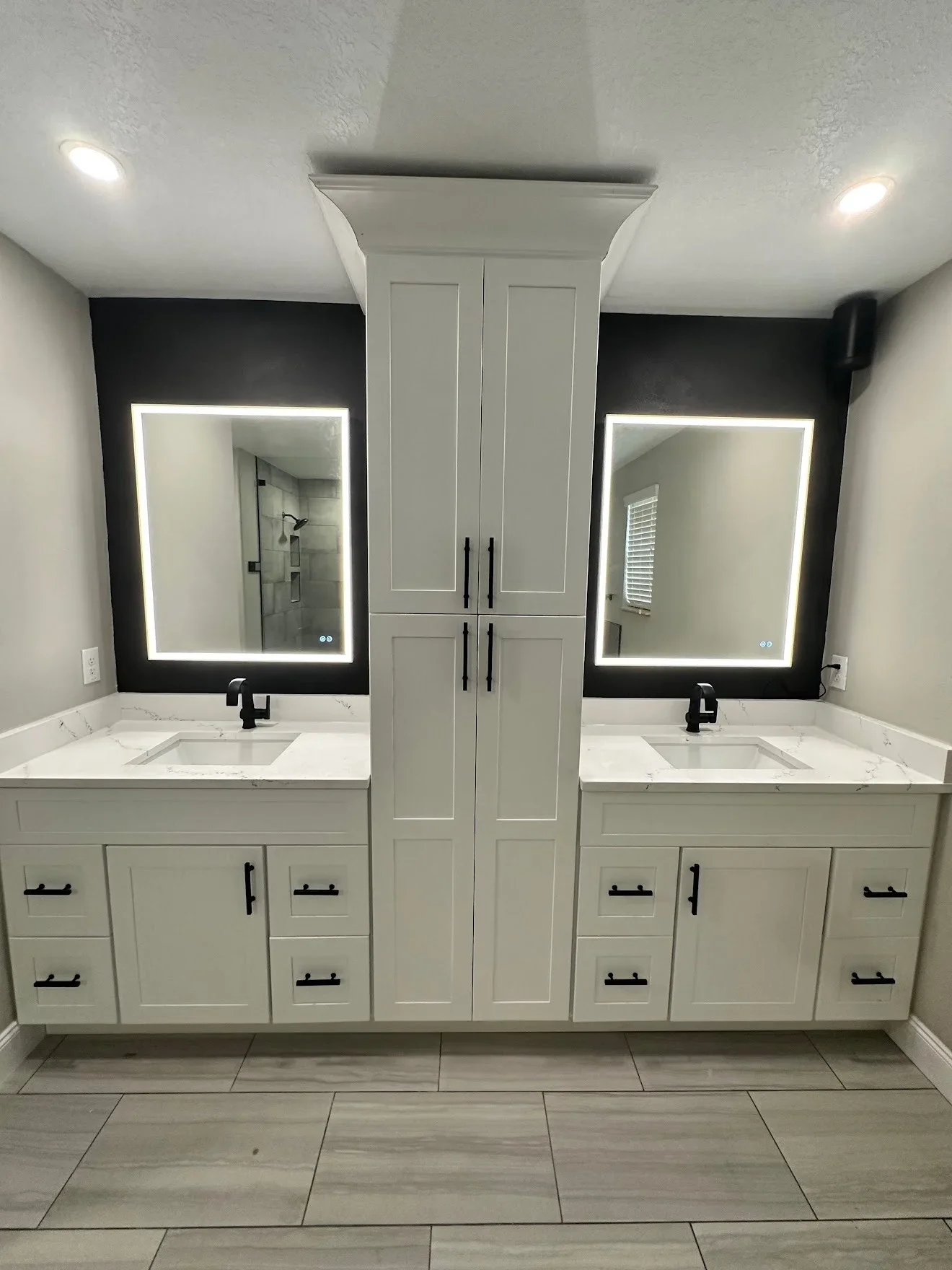 Dual white vanity with marble countertops, LED-backlit mirrors, black hardware, and tile flooring