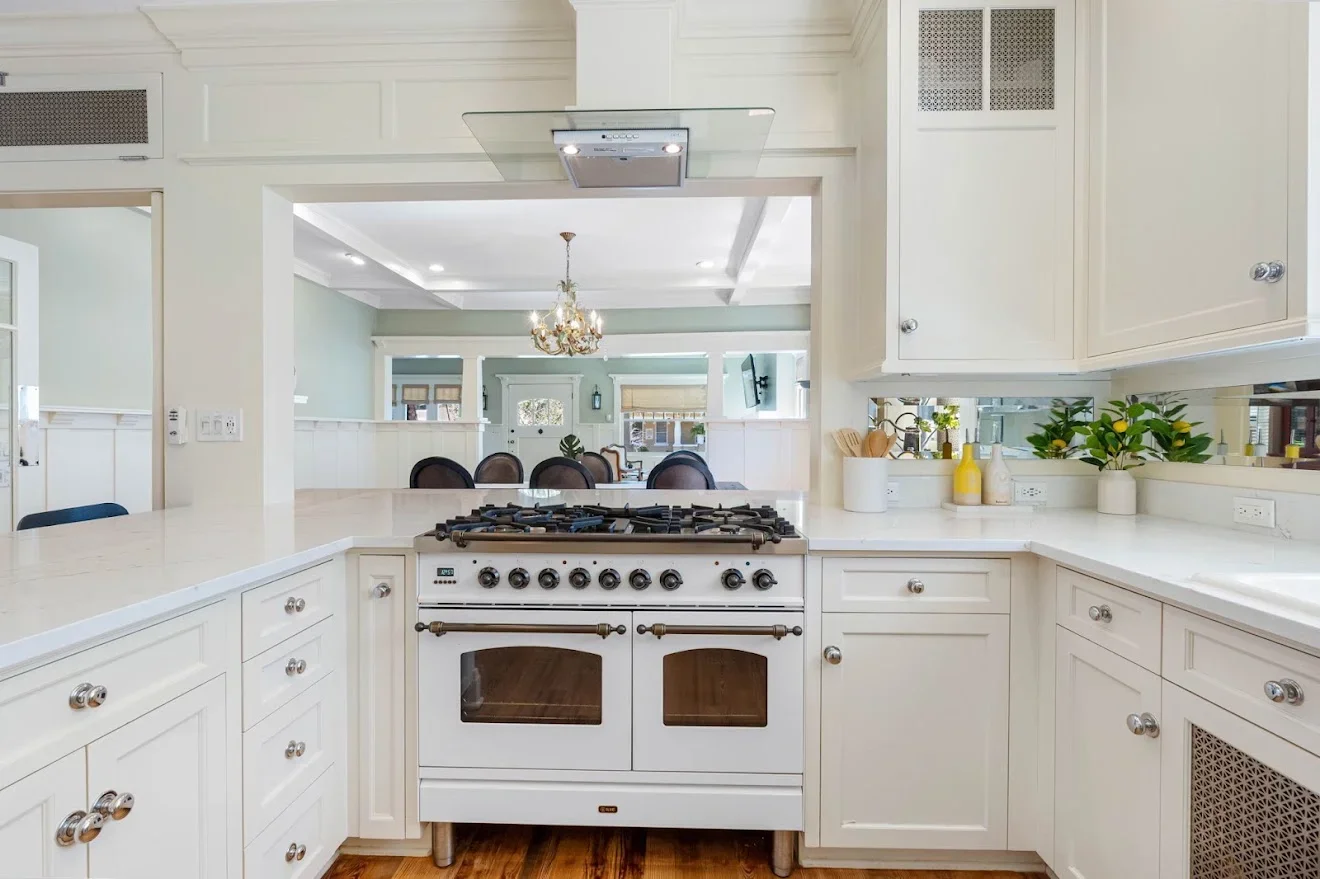 White kitchen with dual ovens, quartz counters, custom cabinetry, and coffered ceiling