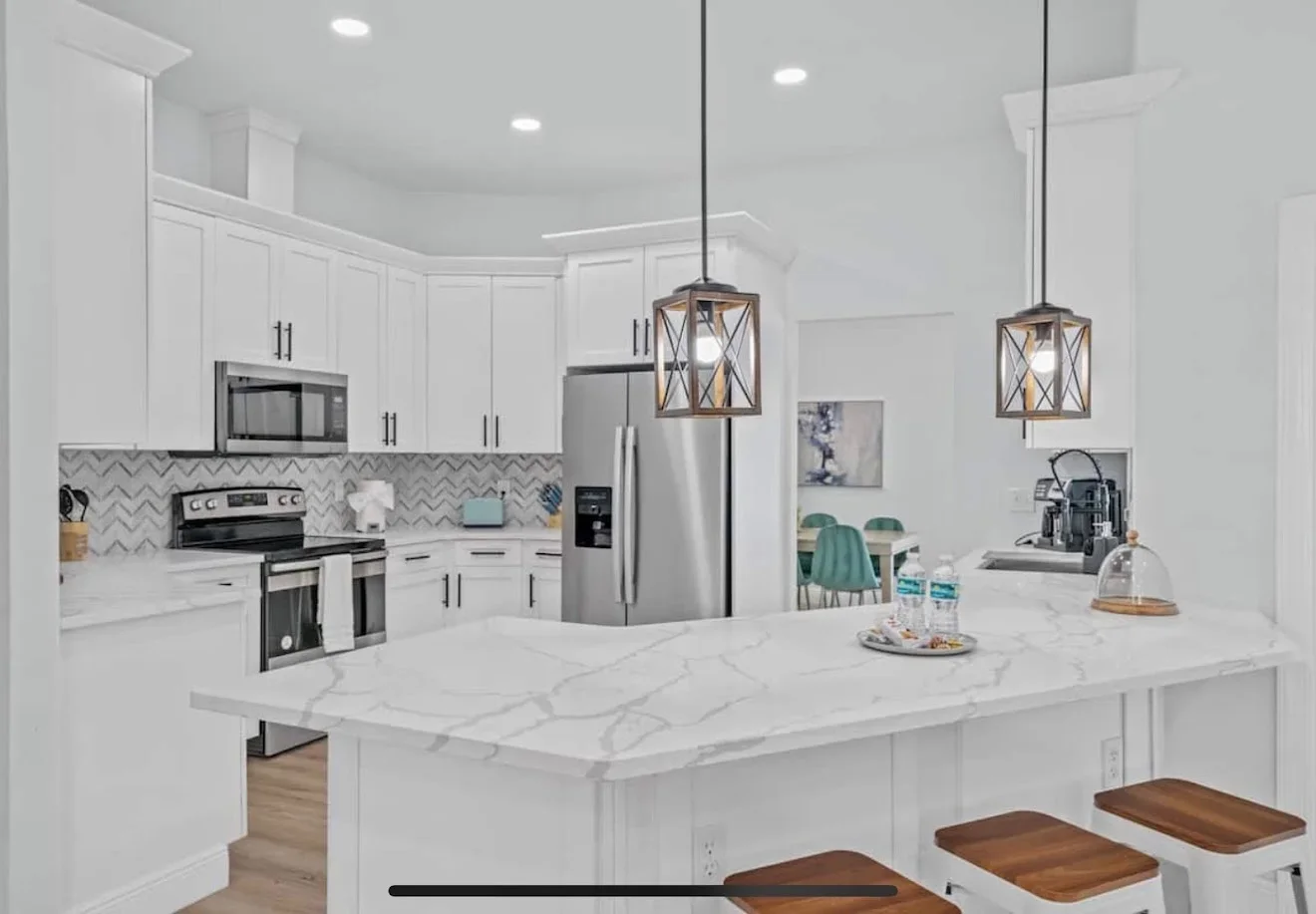 White kitchen with marble island, stainless steel appliances, and herringbone backsplash