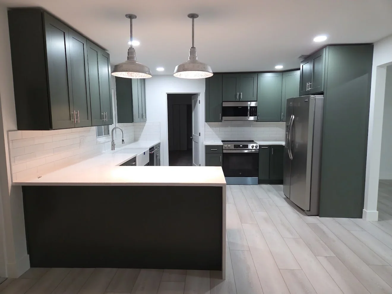 Modern kitchen with dark green cabinets, white quartz counters, stainless steel appliances, and pendant lights