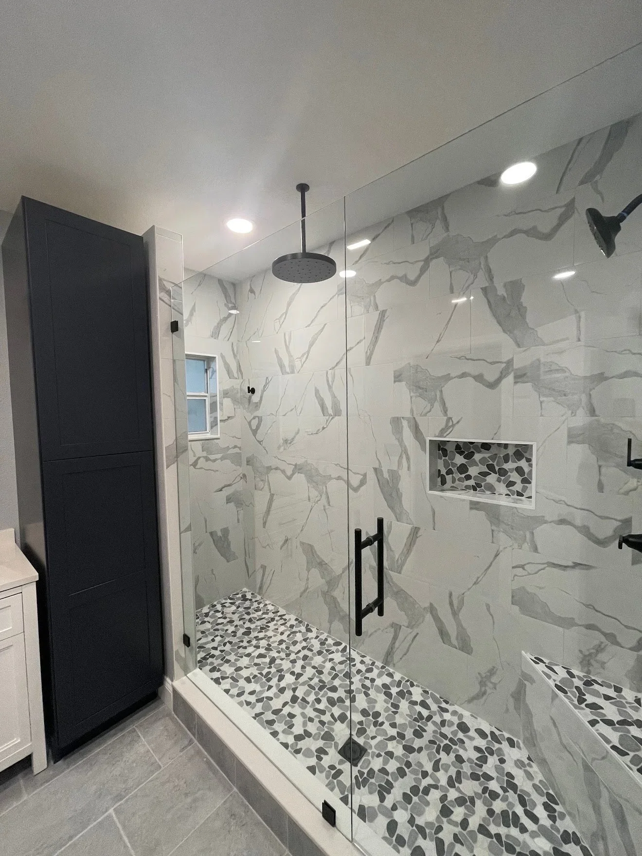 Walk-in shower with marble tile walls, river rock mosaic floor, frameless glass door, and matte black fixtures