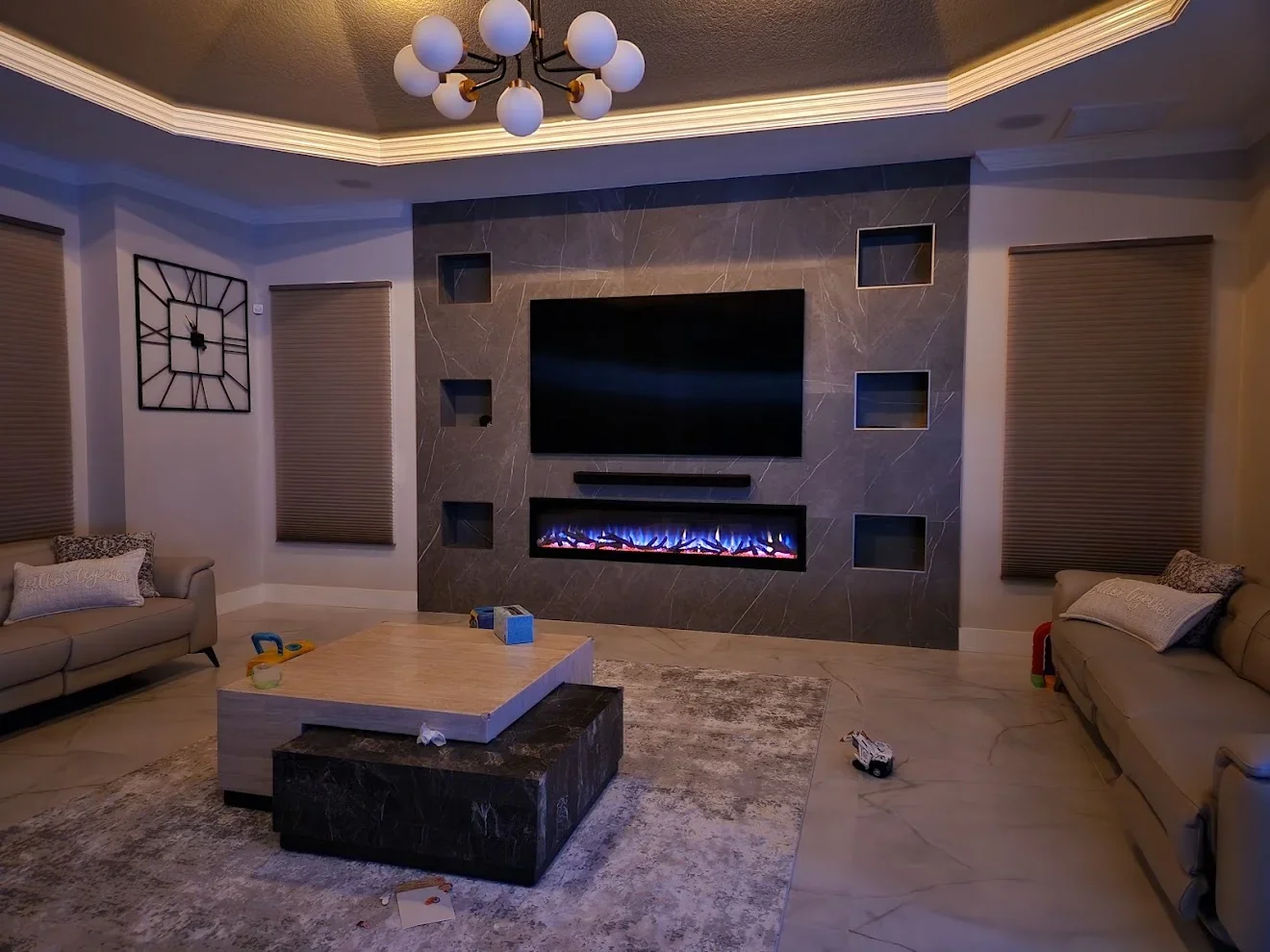 Modern media room with marble accent wall, electric fireplace, recessed shelving, and tray ceiling lighting