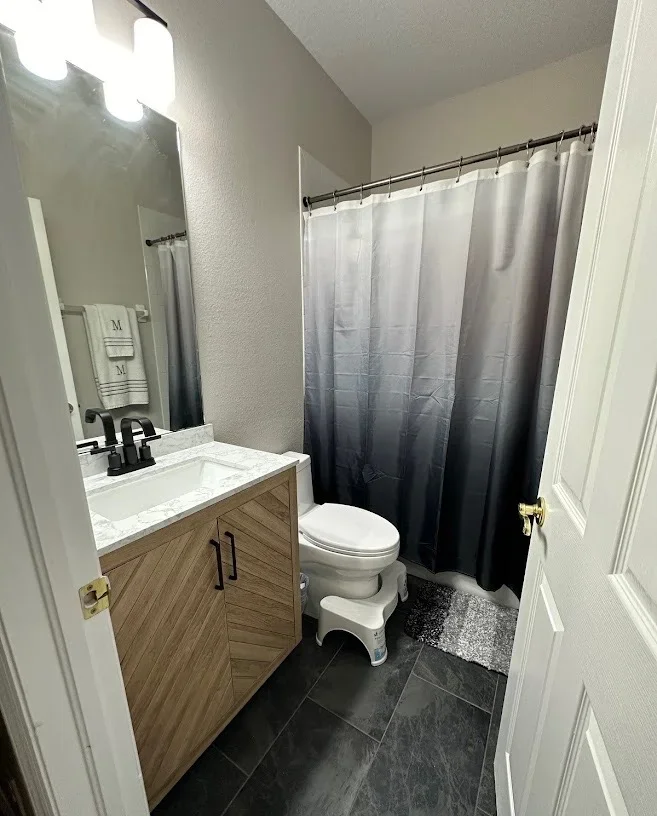 Bathroom with wood vanity, marble countertop, dark tile flooring, and ombre shower curtain