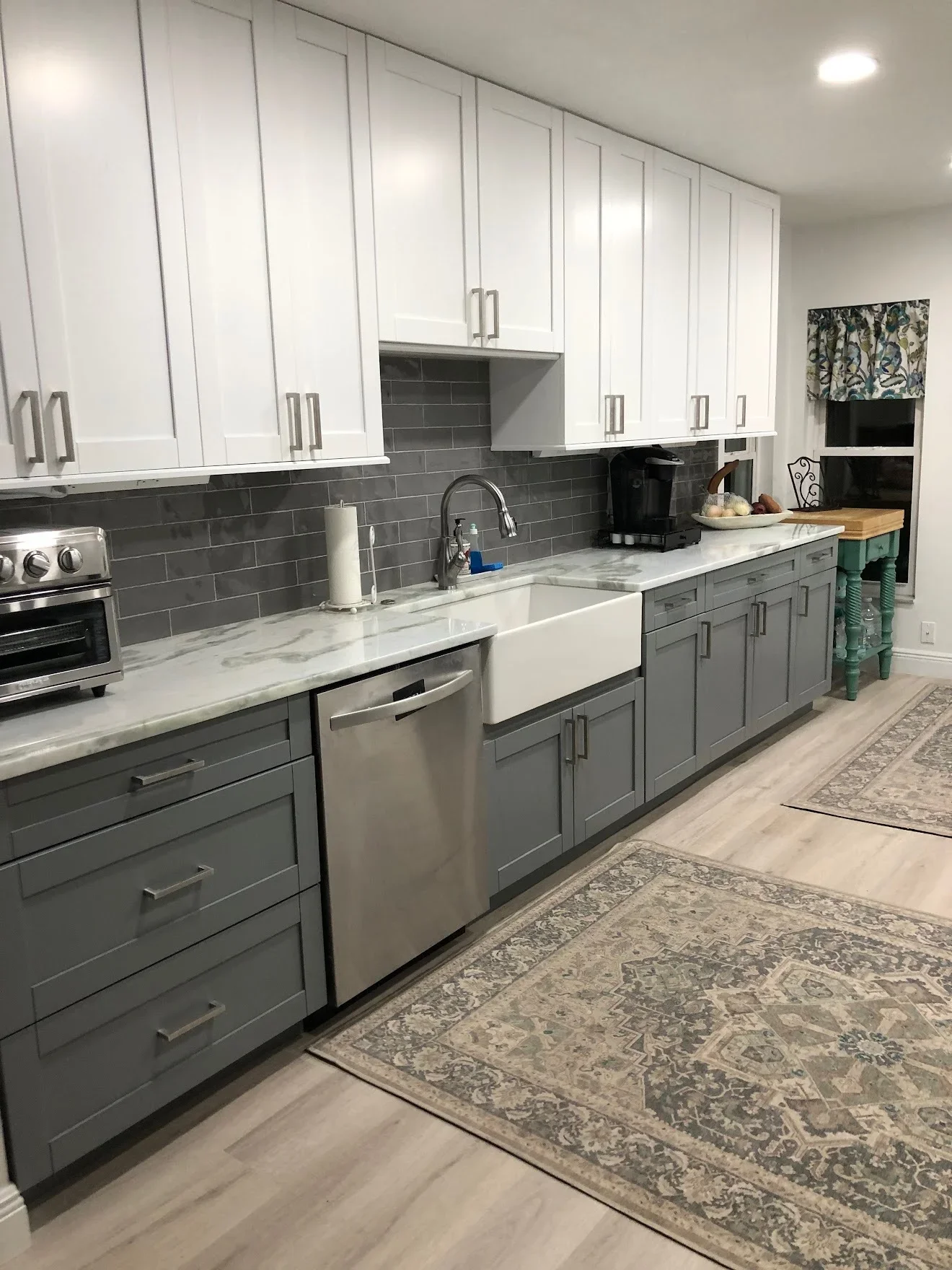 Two-tone kitchen with white upper and gray lower cabinets, marble counters, subway tile backsplash, stainless appliances