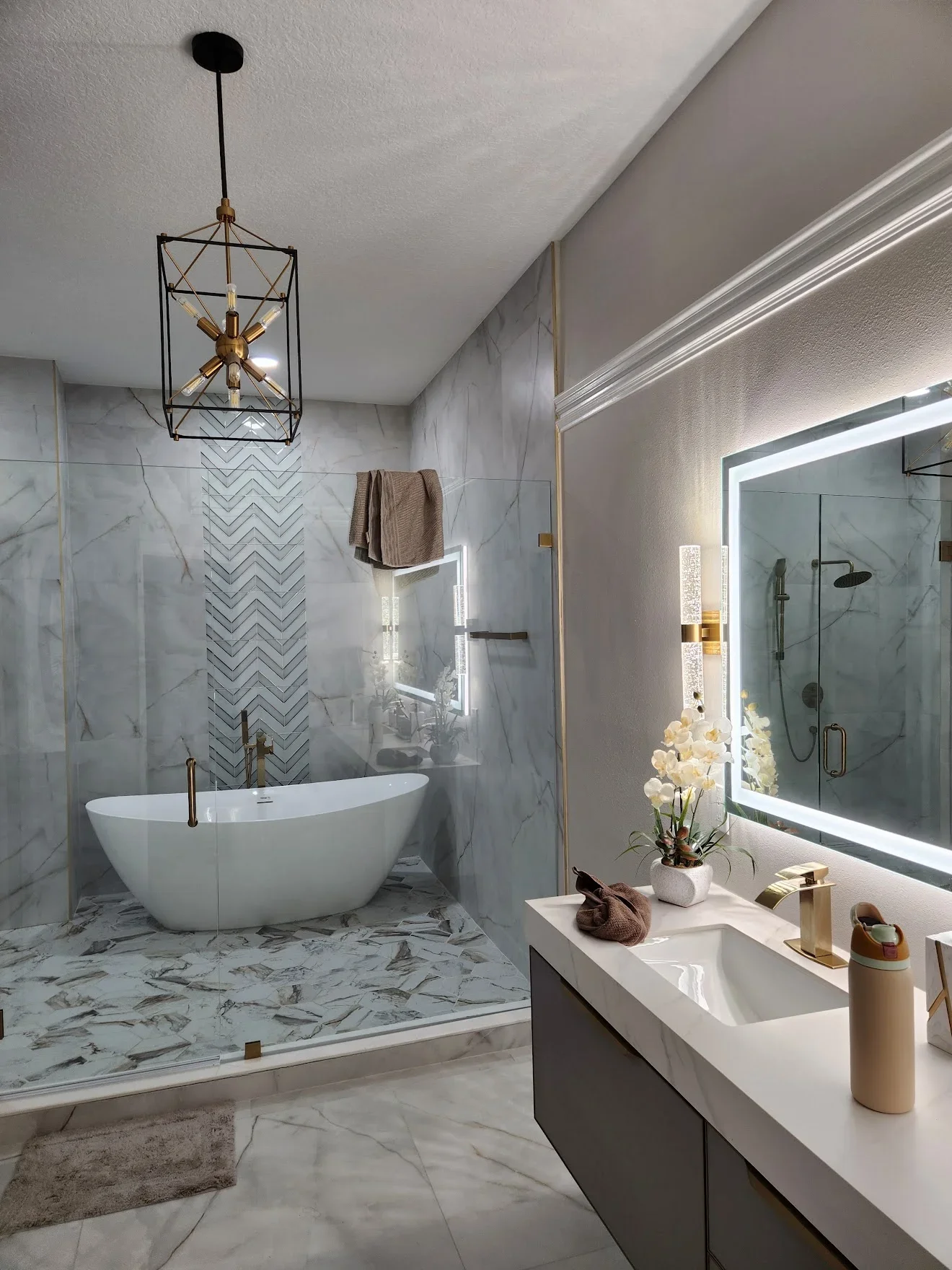 Marble bathroom with freestanding tub, herringbone tile accent, LED mirror, and glass shower enclosure